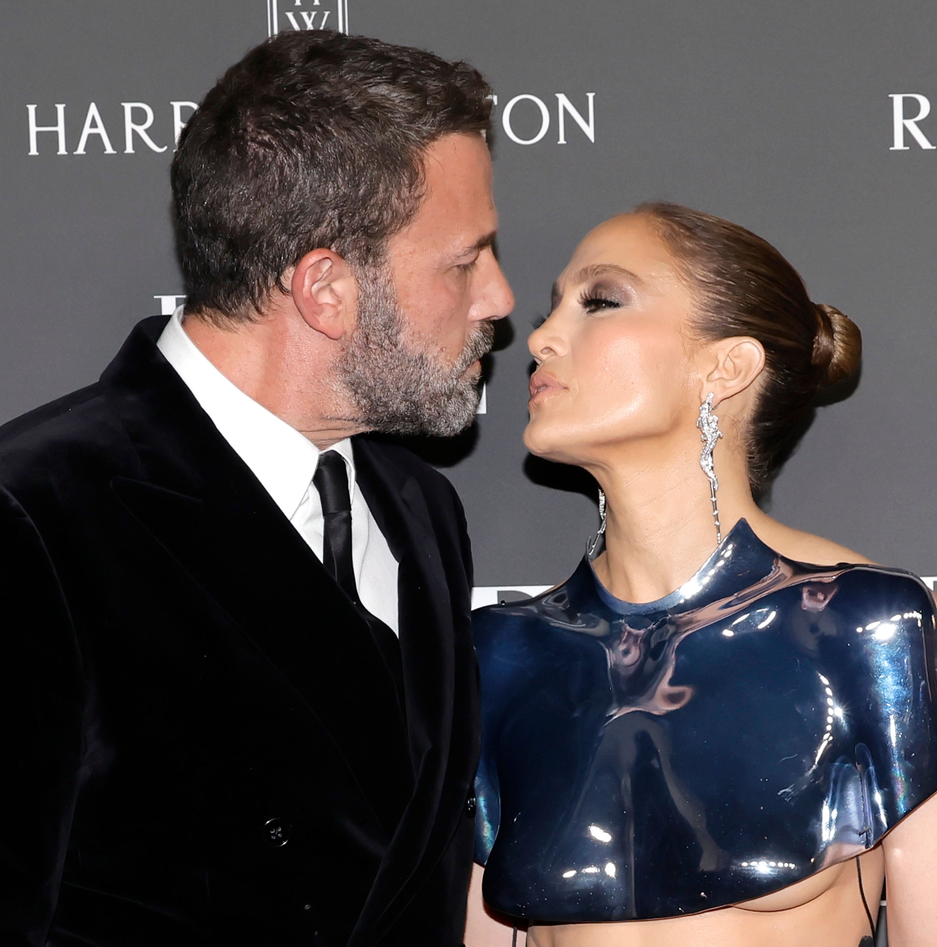 Ben Affleck and Jennifer Lopez in formal attire as they lean in for a kiss on the red carpet at an event