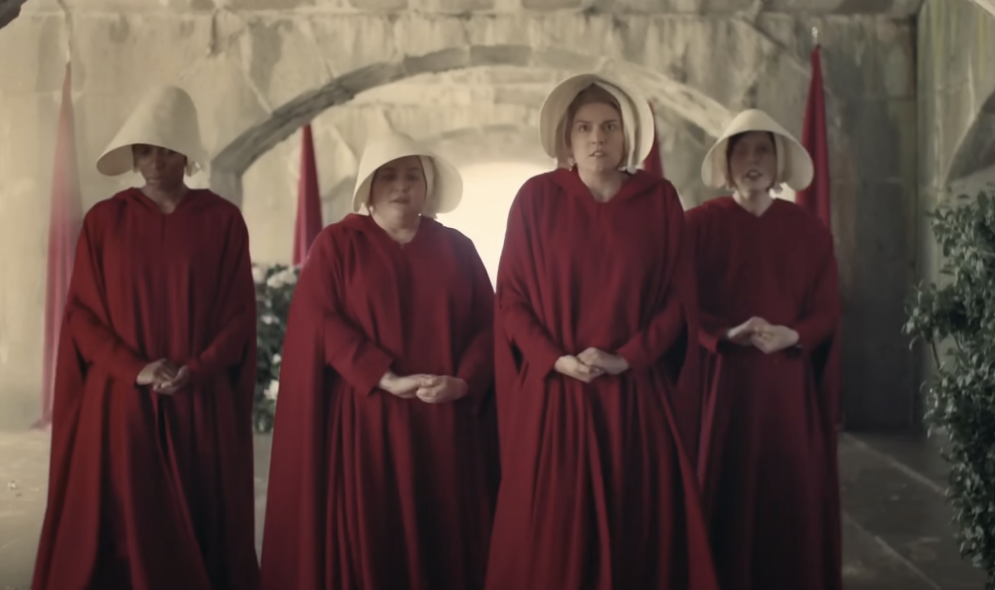 Kim Kardashian, another notable name, and two unidentified women wear red cloaks and white bonnets, reminiscent of outfits from &quot;The Handmaid's Tale,&quot; standing solemnly