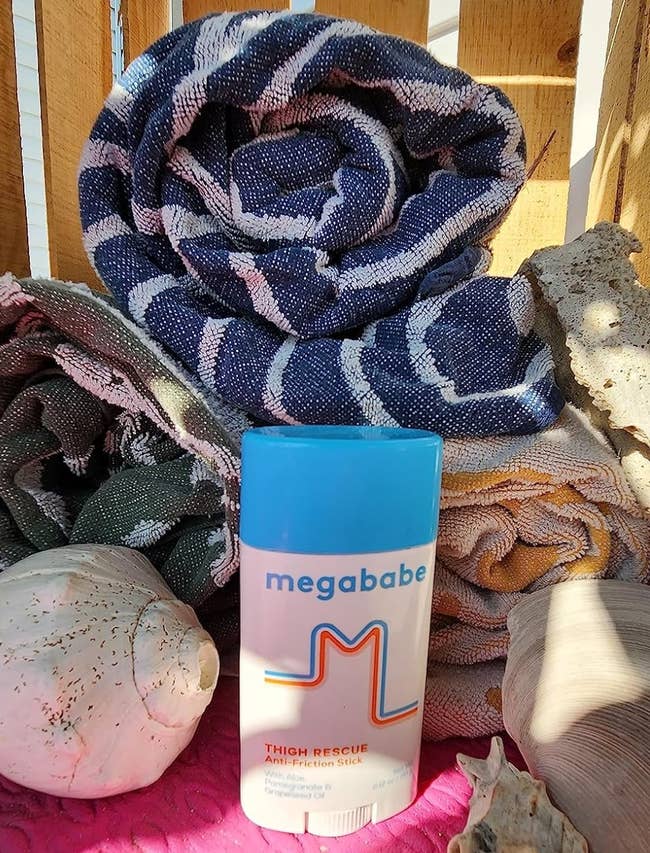 Megababe Thigh Rescue stick displayed with towels and seashells in the background