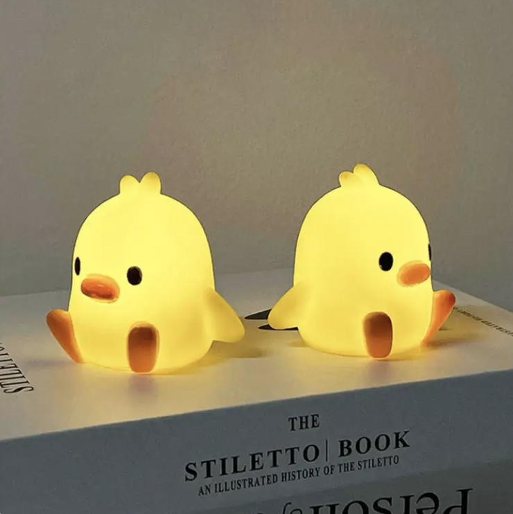 Dos luces nocturnas en forma de pollito sobre un libro titulado "The Stiletto Book: An Illustrated History of the Stiletto"