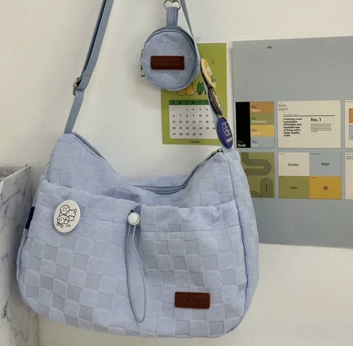 Bolso de hombro acolchado colgado en la pared con un llavero pequeño y parche decorativo de un dibujo caricaturesco de un perro. Fondo con calendario y cuadros de colores