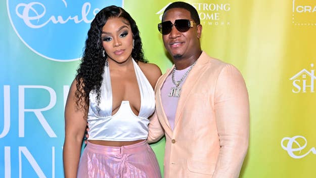 Kendra Robinson and Yung Joc pose together on a red carpet, with Yung Joc wearing a beige suit and sunglasses, and Kendra wearing a silver top and pink pants