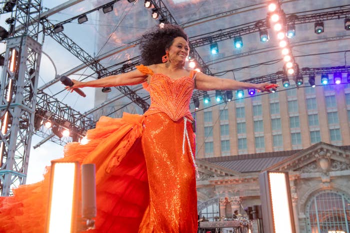 Diana Ross performs connected  signifier    wearing a sparkling sequined gown with a ruffled train, arms outstretched. The backdrop includes a gathering  and lawsuit   lighting