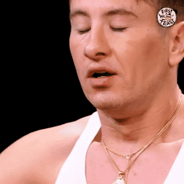 Barry Keoghan winces with eyes closed, wearing a white tank top and gold necklaces on &quot;First We Feast.&quot;