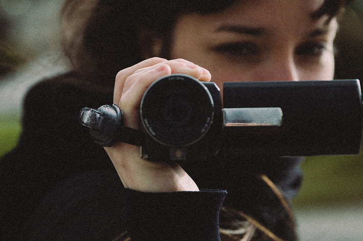 人物がビデオカメラを持って撮影しているシーン。風景の一部がぼやけて背景に見える。