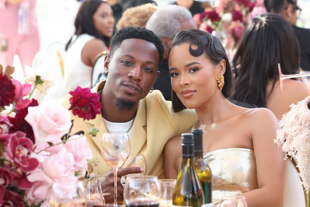 Joey Bada$$ and Serayah pose together at a formal event with floral decorations and wine bottles on the table