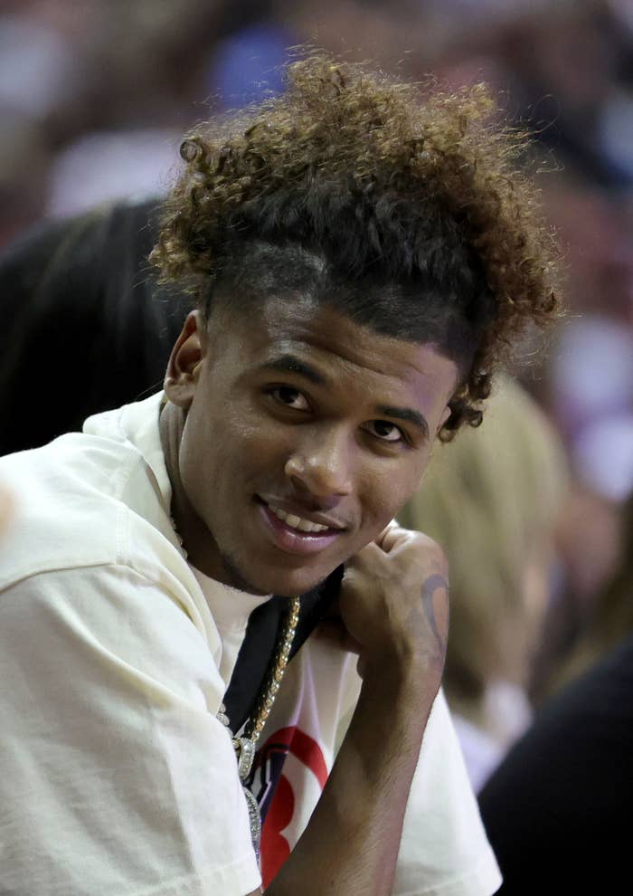 Jalen Green smiles while seated with a crowd in the background. He wears a short-sleeve shirt and a chain necklace