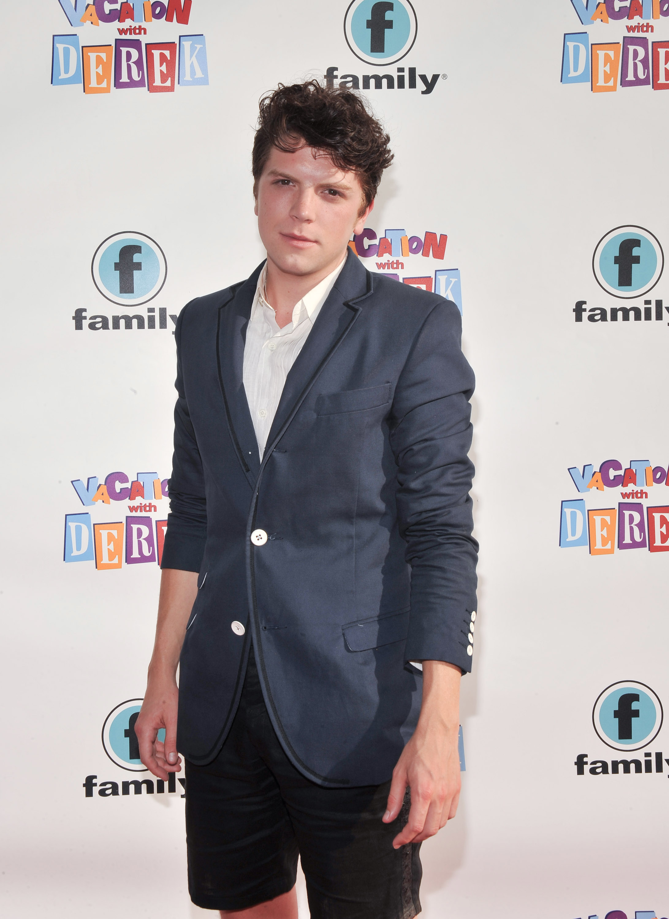 Michael Seater on the red carpet in a casual blazer with black shorts takes a photo at an event.