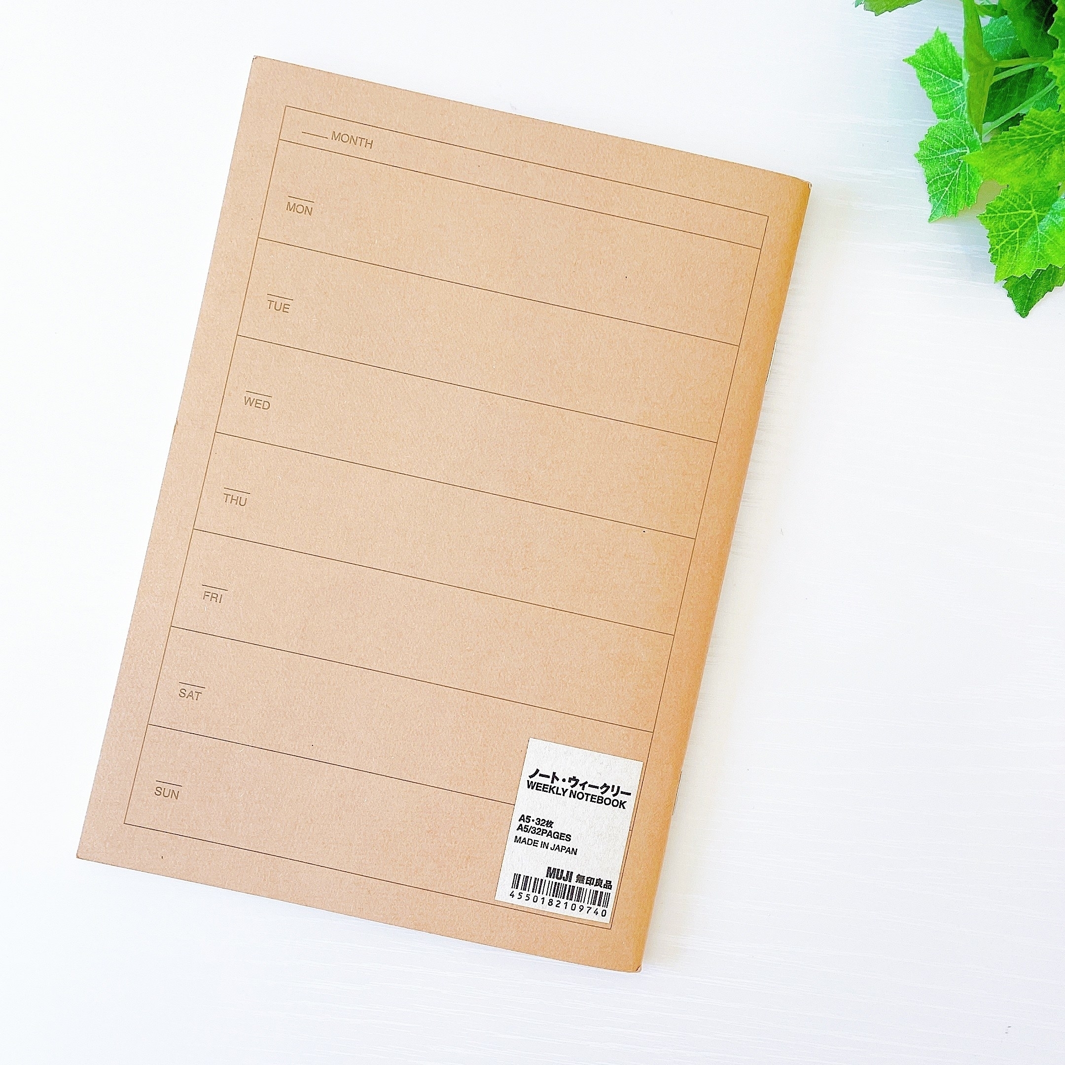 無印良品の週間スケジュールノートブックが白い背景と緑の植物の隣に置かれている。