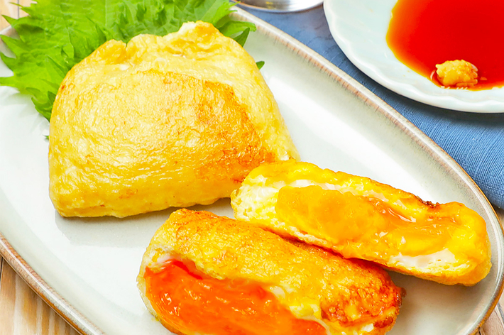 お皿に乗った揚げ豆腐が3つあり、切り口からはチーズとトマトソースが見える。隣に醤油が入った小皿と飲み物が置かれている。