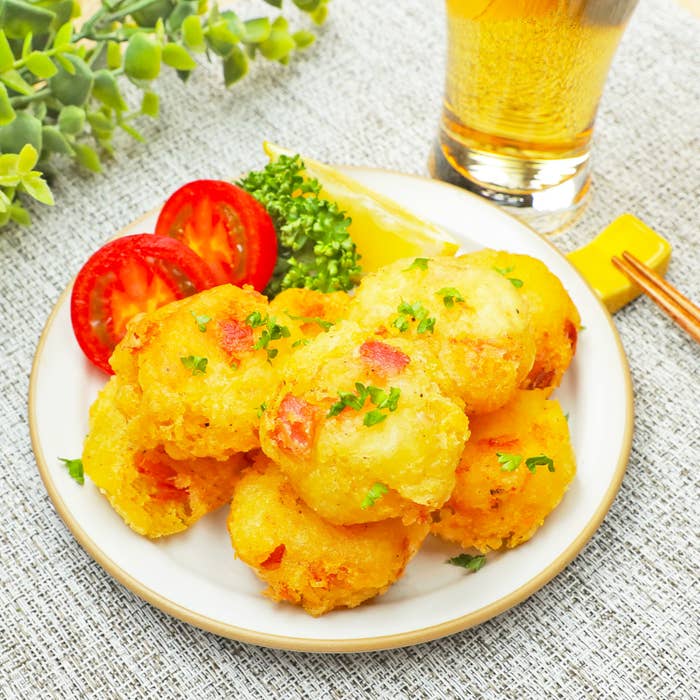 お皿に盛られたゴールデンポテトのフライ、トマト、ピクルス、パセリ、そしてグラスビール。
