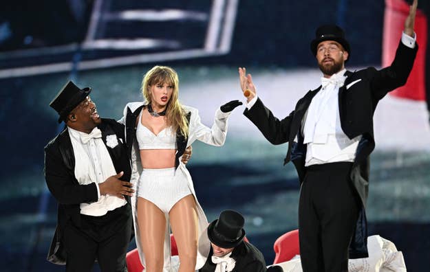 Taylor Swift performs on stage in a white outfit with two male dancers in black and white formal wear during a music event