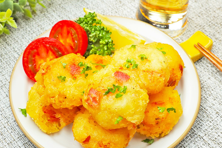 皿に乗ったポテトコロッケ、スライストマト、パセリとレモンのクォーター。隣にはグラスに注がれたビールが置かれている。