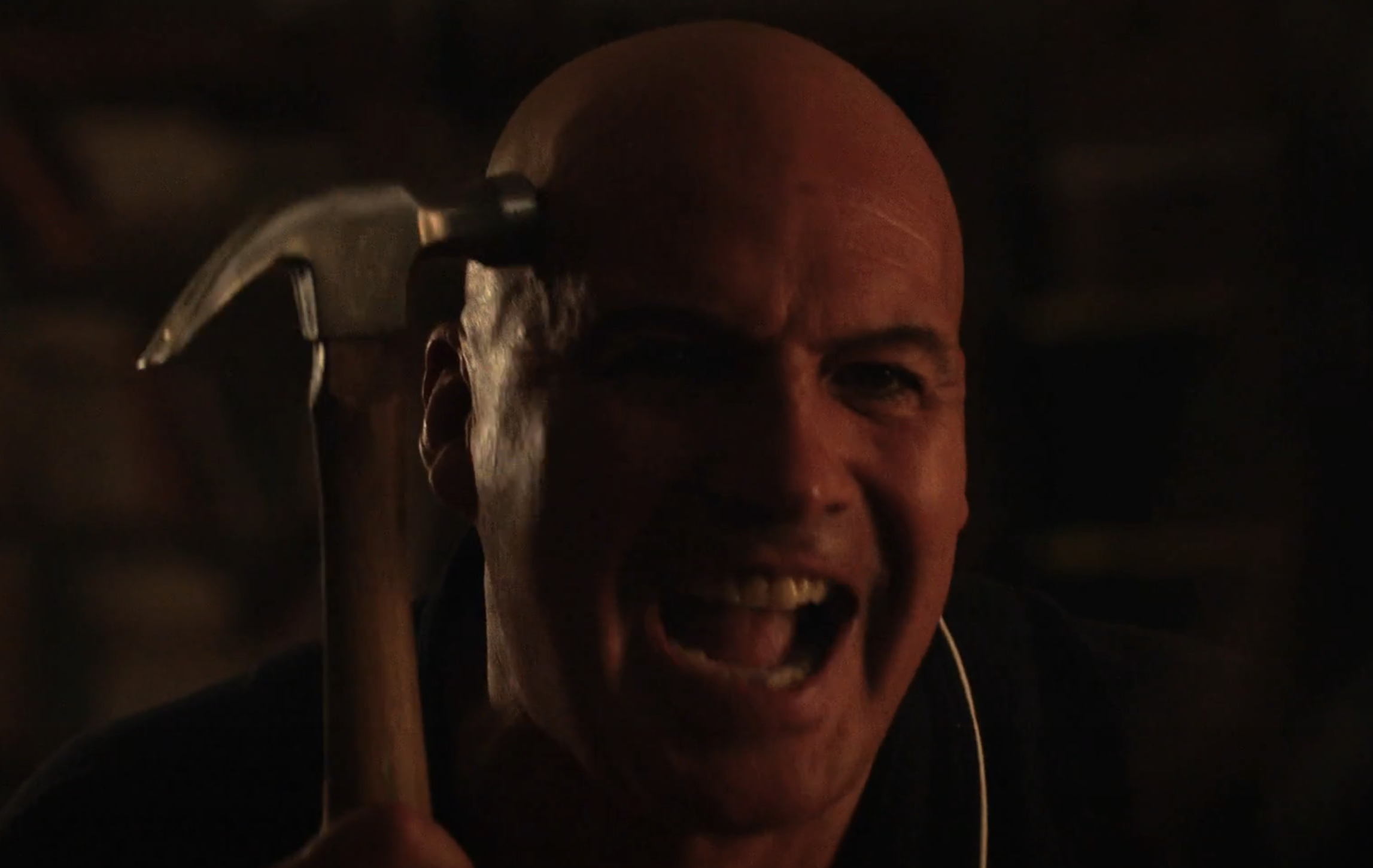 Billy Zane as Larry Ray holding a hammer up to his head