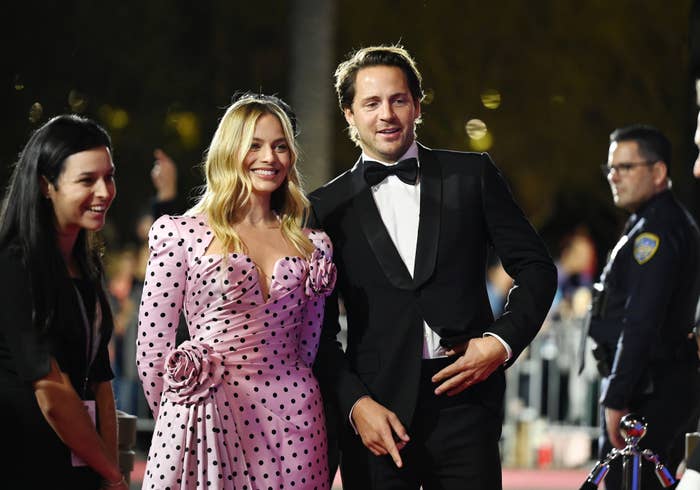 Margot Robbie in a polka dot dress and Tom Ackerley in a tuxedo pose on the red carpet