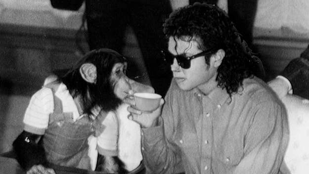 Michael Jackson in a casual shirt and sunglasses drinks tea while sitting next to a chimpanzee dressed in overalls and a striped shirt