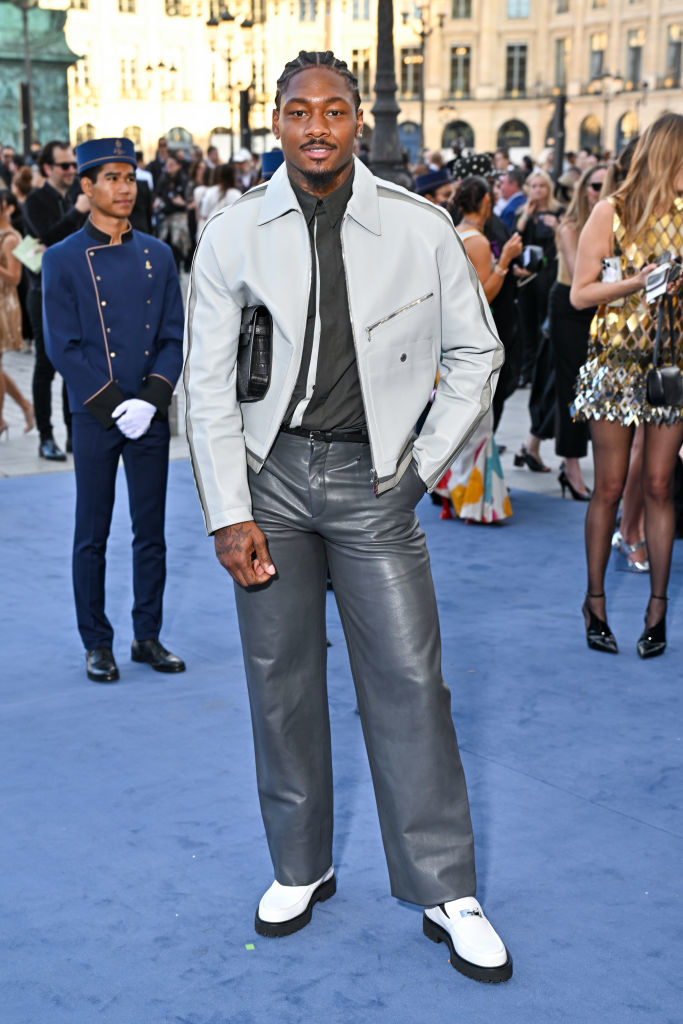 Stefon Diggs wears a sleek, modern outfit with a light jacket and leather pants, posing at a formal event