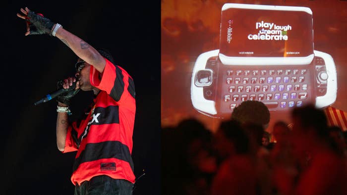 Travis Scott performing on stage with a microphone. Behind him is a projection with a phone displaying the words &quot;play laugh dream celebrate.&quot;