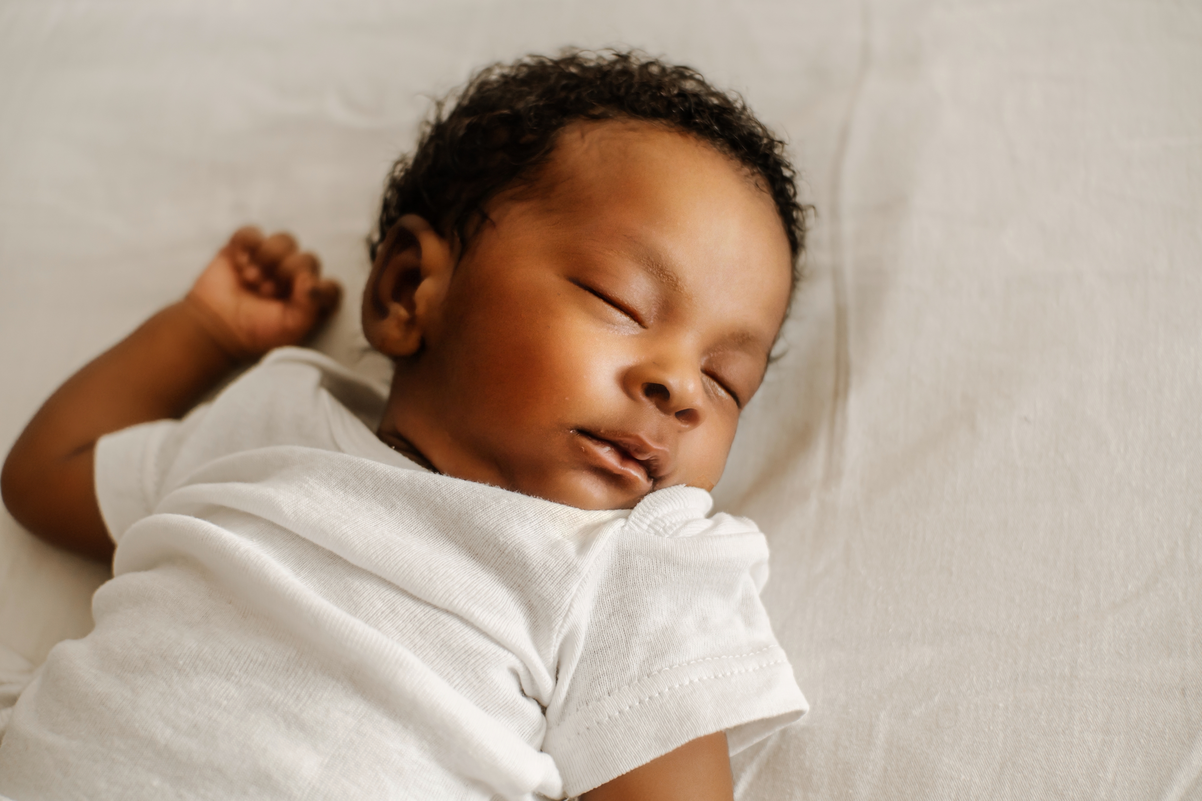 A baby sleeps peacefully on a soft surface, wearing a simple white outfit