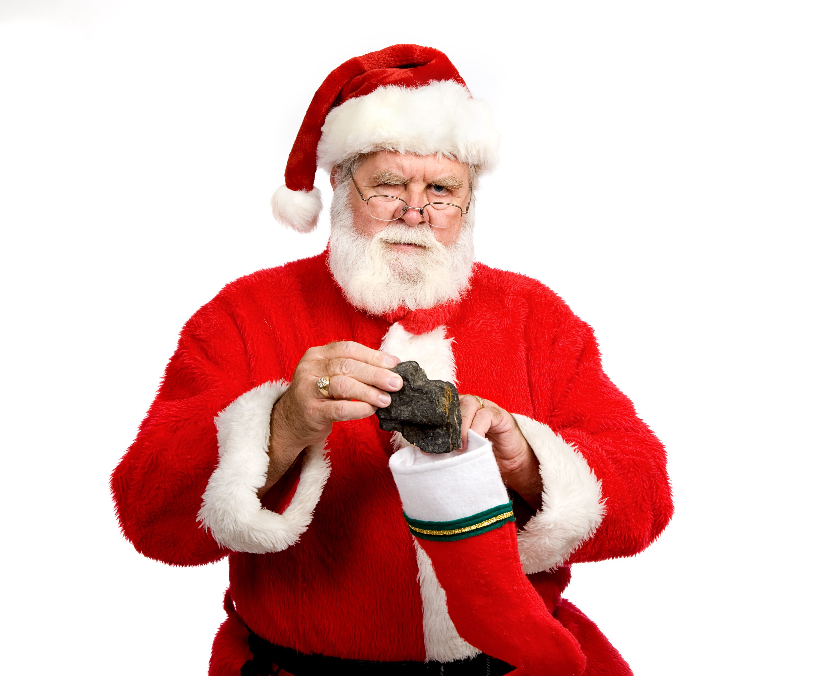 Santa Claus holding a piece of coal above a red Christmas stocking against a white background. Santa appears displeased