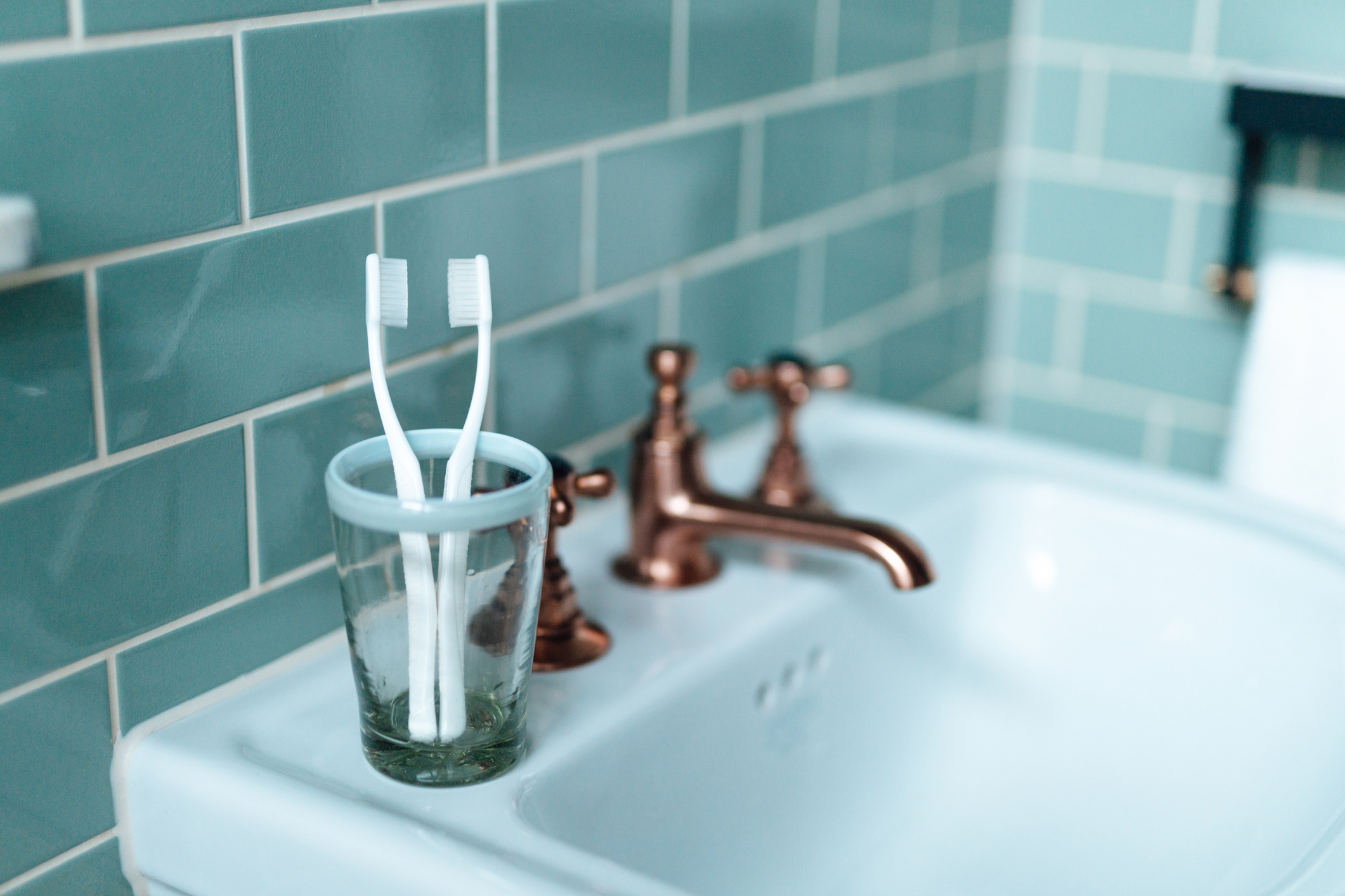 Two toothbrushes in a glass cup on a bathroom sink with bronze faucet fixtures