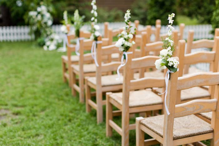 Rows of wooden chairs with floral decorations are set up outdoors, suggesting a wedding or romantic event