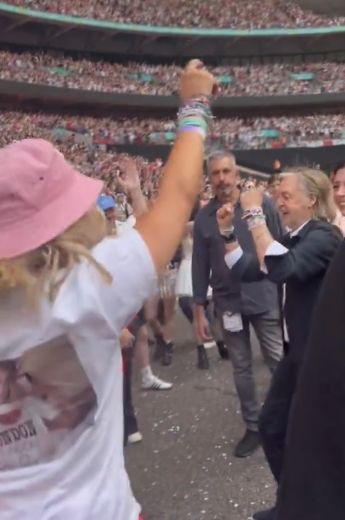 Paul McCartney is greeted and celebrated by excited fans at a concert, with a woman in the foreground wearing a hat and many bracelets