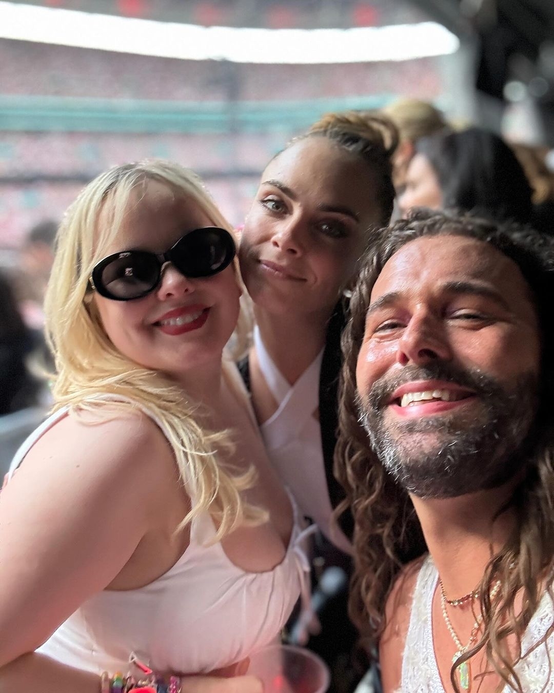 Jonathan Van Ness, Nicola Coughlan, and Cara Delevingne pose together at an event, all three smiling. Nicola wears black sunglasses, and Jonathan has long hair