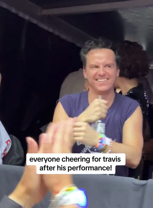 Andrew Scott cheers with a crowd for Travis after his performance, holding a water bottle, wearing a sleeveless shirt and bracelets