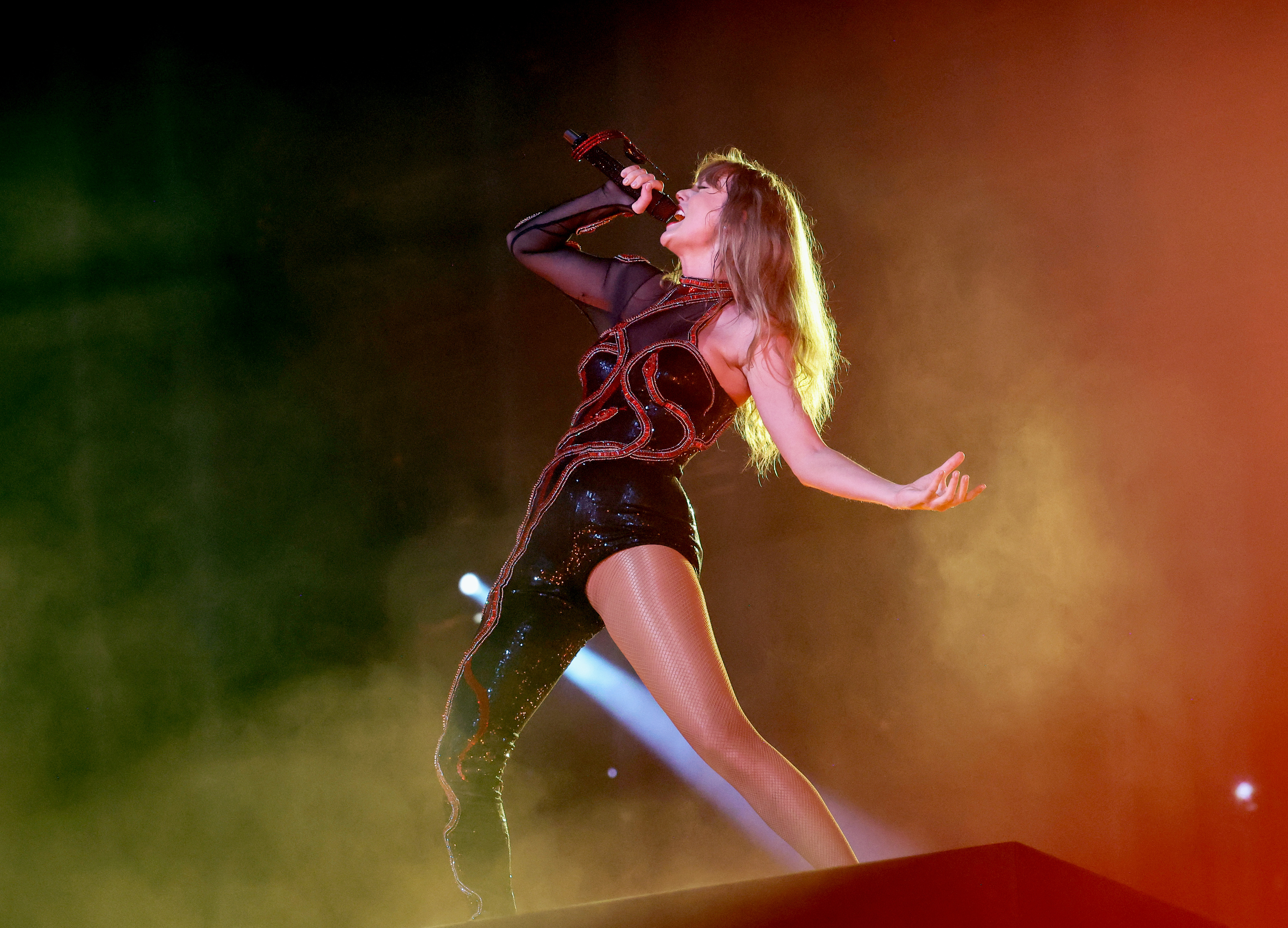 Taylor Swift singing passionately on stage, wearing a sparkling one-sleeve bodysuit with intricate designs