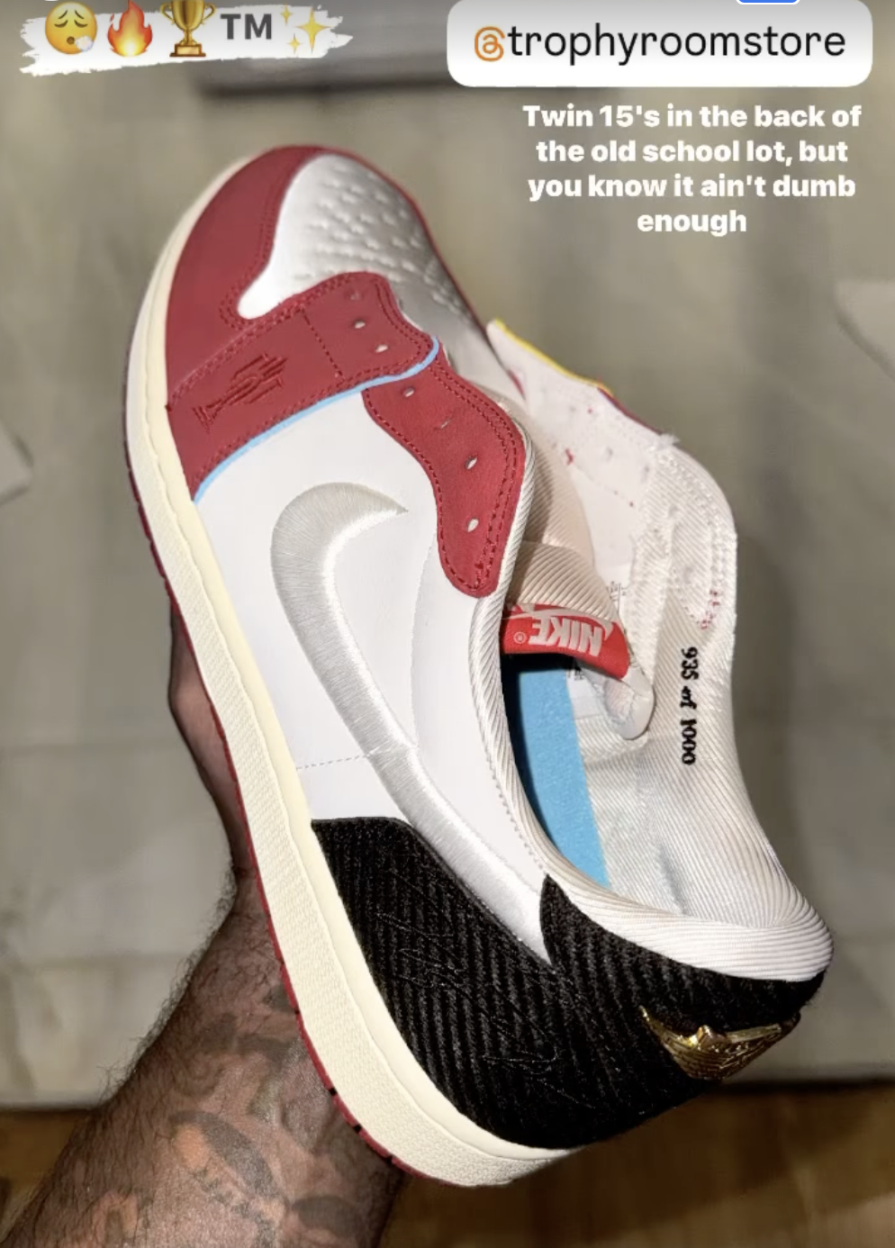 A hand holds a stylish sneaker with red, white, and black details. The @trophyroomstore Instagram username and text &quot;Twin 15&#x27;s in the back of the old school lot, but you know it ain&#x27;t dumb enough&quot; are visible