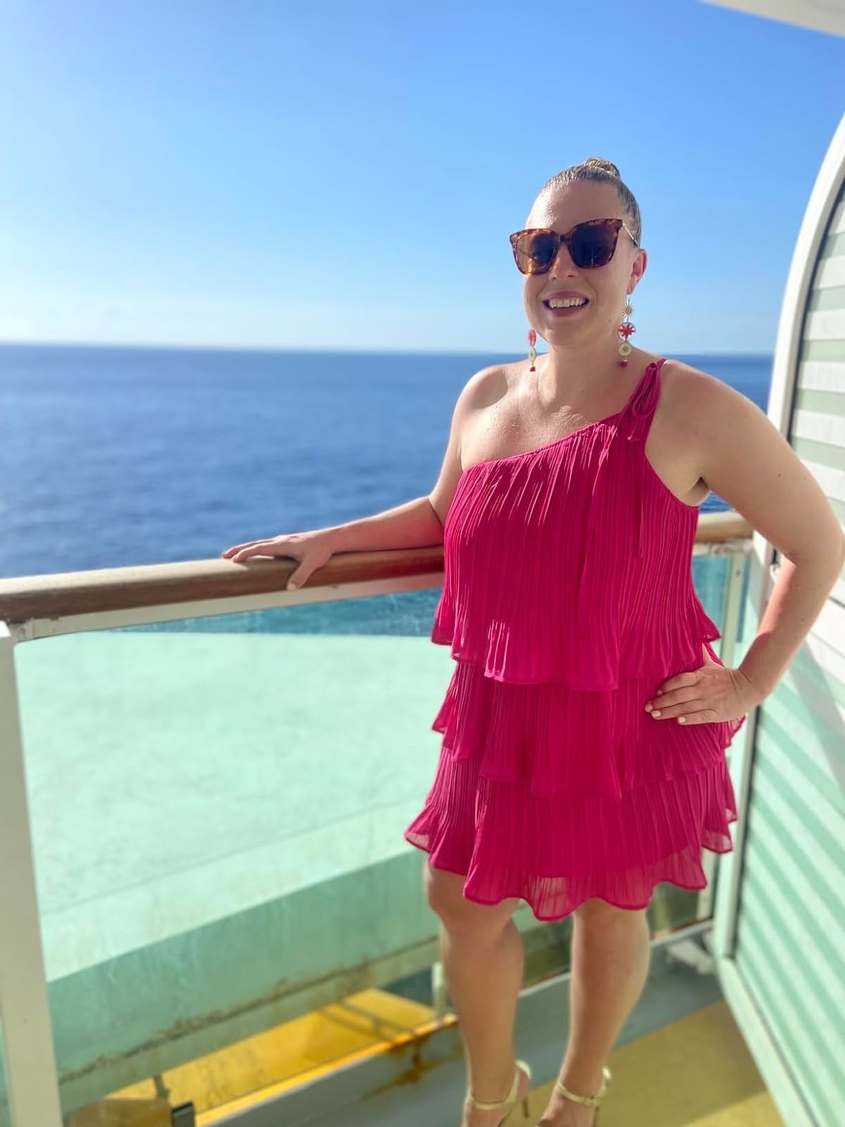 Person in a tiered, sleeveless dress smiling on a ship deck with the ocean in the background