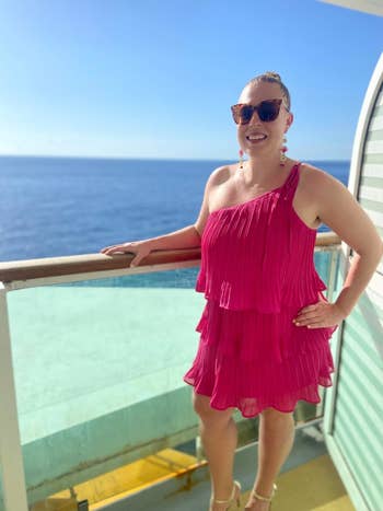 Person in a tiered, sleeveless dress smiling on a ship deck with the ocean in the background