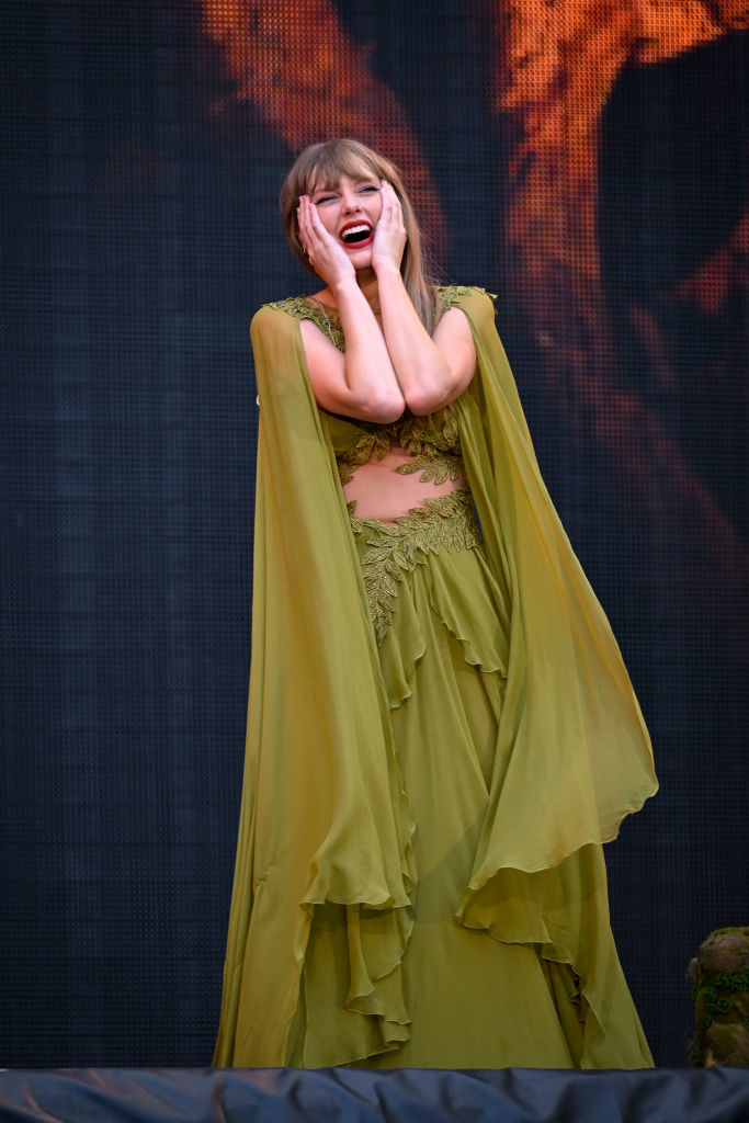 Taylor Swift on stage in an elegant dress, mid-performance with a surprised expression on her face