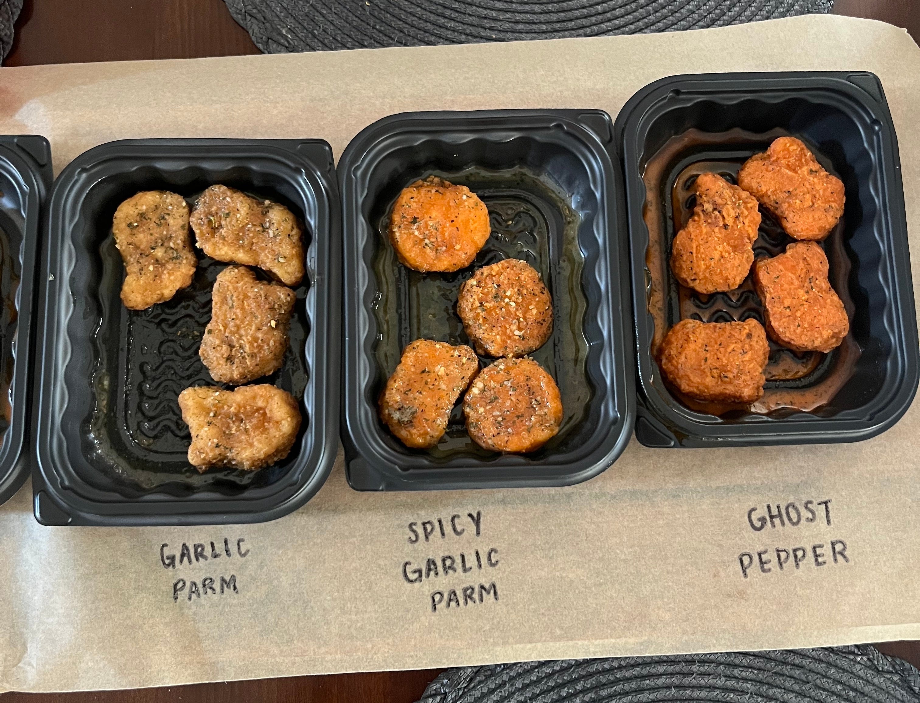 Three trays of chicken wings labeled 'Garlic Parm,' 'Spicy Garlic Parm,' and 'Ghost Pepper' are displayed on a table