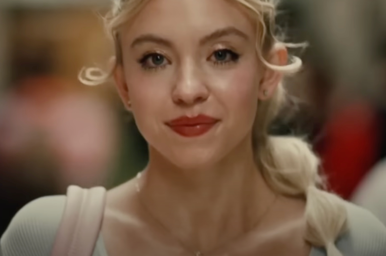 Sydney Sweeney close-up portrait smiling, wearing a casual outfit with a light-colored top and hair tied back, in an article for Sex & Love