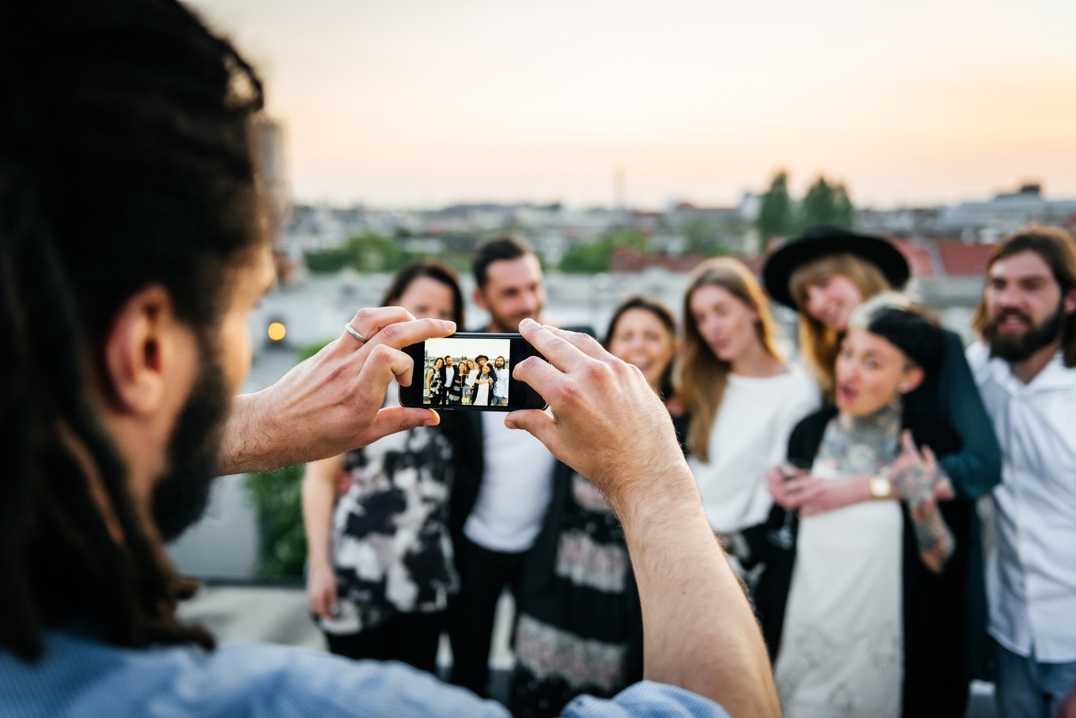 A group of six people posing for a rooftop selfie, dressed in casual clothes. The person taking the selfie is not visible. Names of individuals unknown