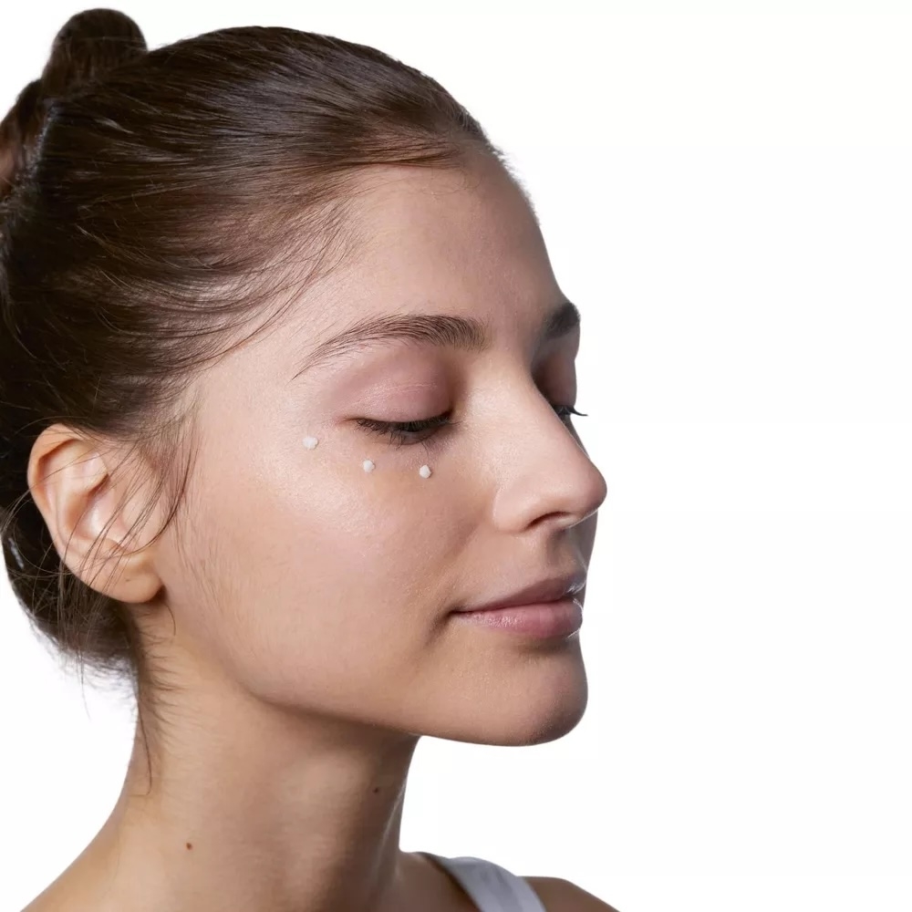 Side profile of a model with her hair in a bun applying skincare dots under her eyes