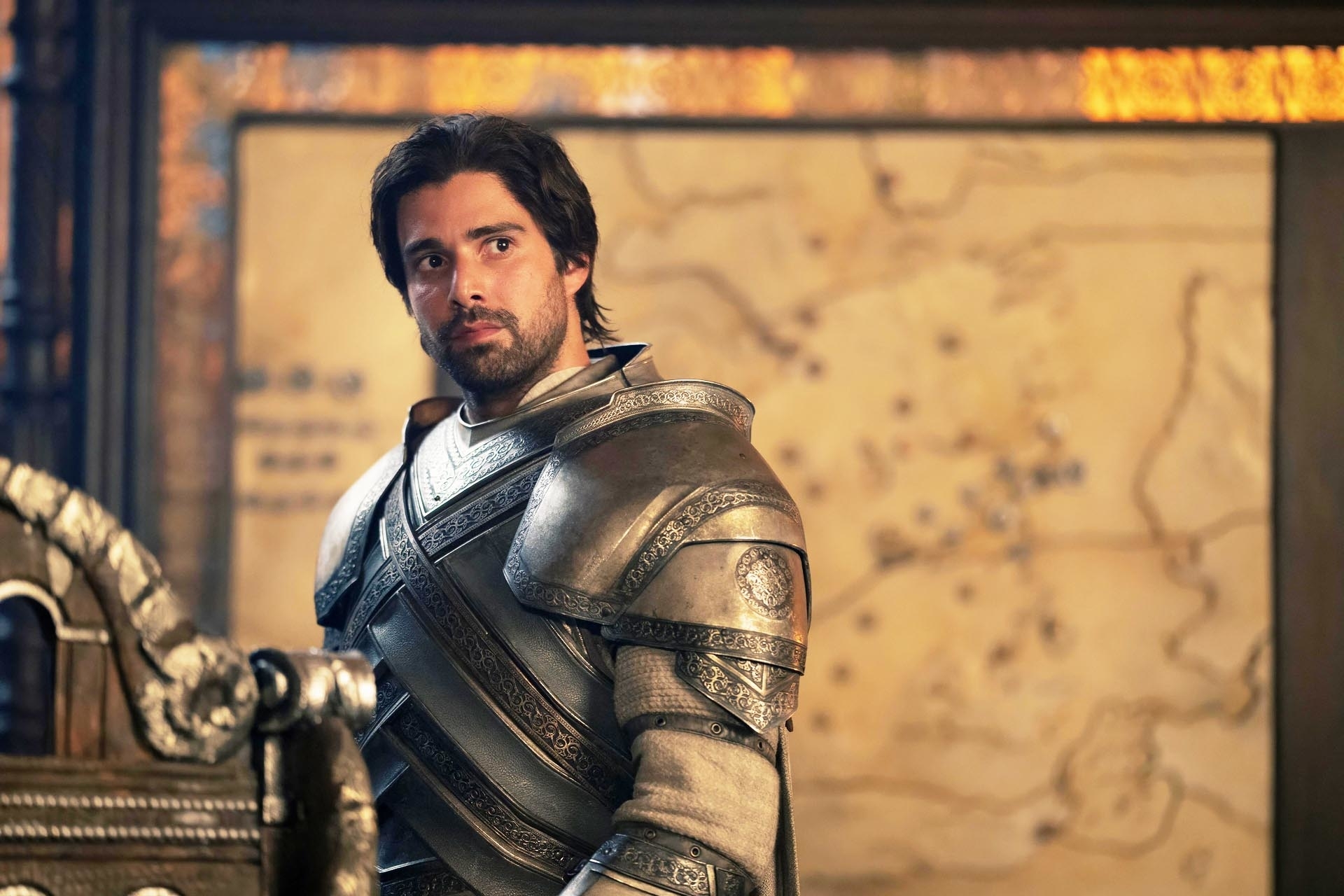 Fabien Frankel, dressed in medieval knight armor, stands in front of a map, portraying a character from a TV series