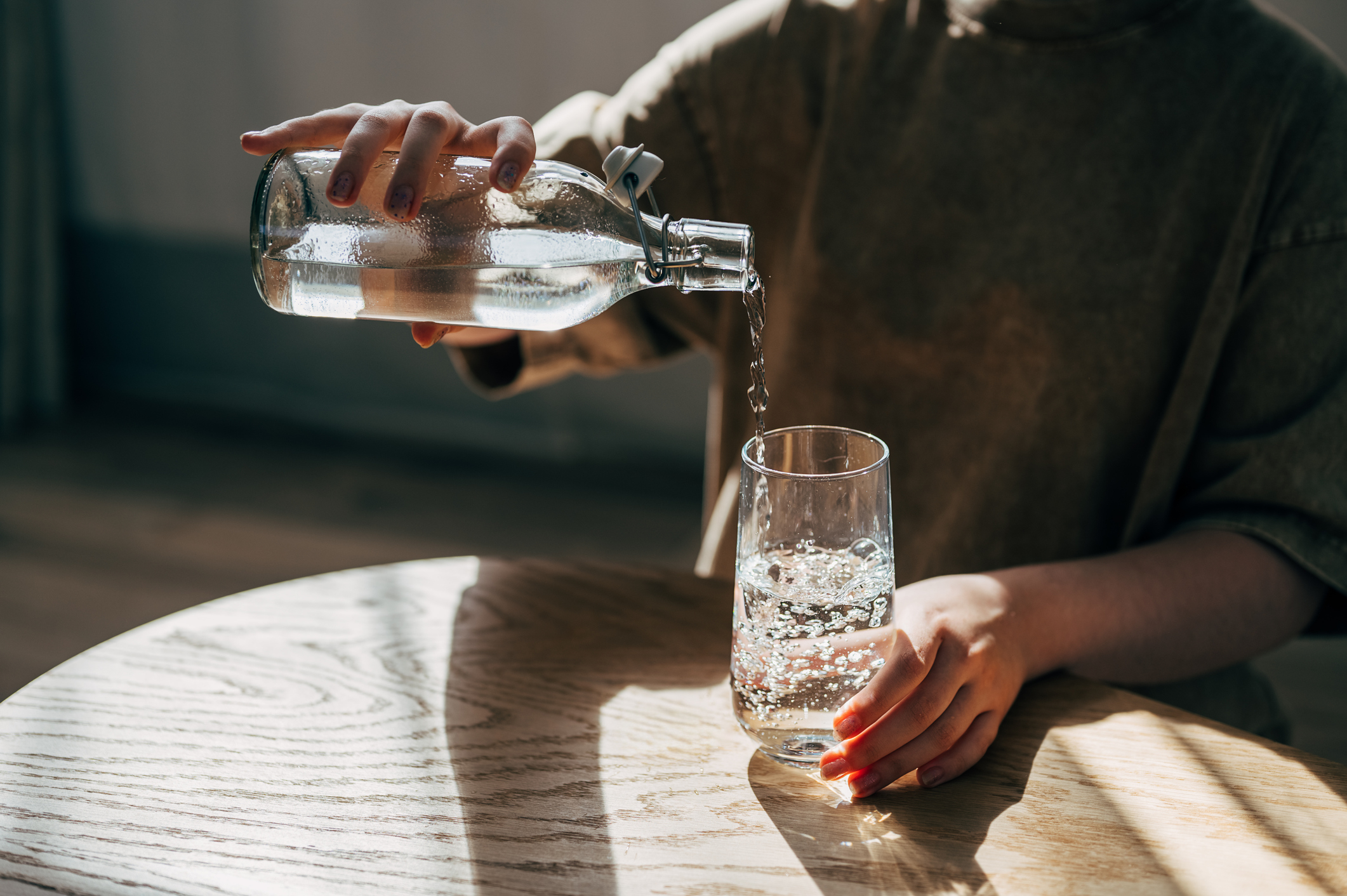 Person pouring water from a bottle into a glass at a wooden table