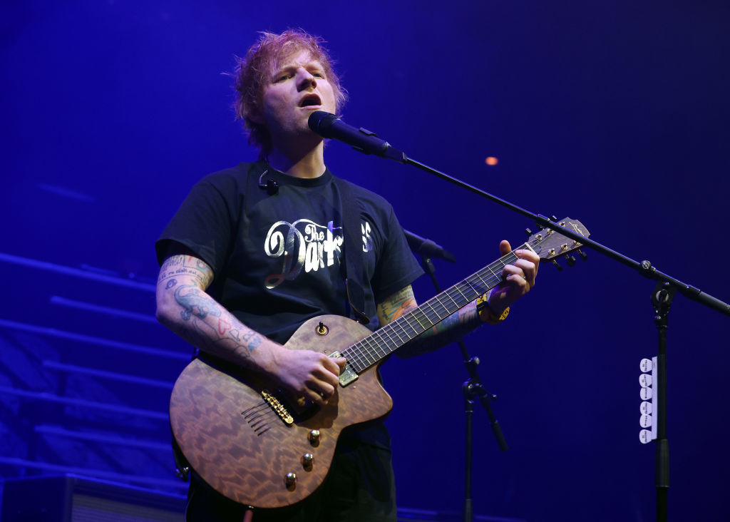 Ed Sheeran performs passionately on stage with a guitar in hand, wearing a casual t-shirt, during a live concert