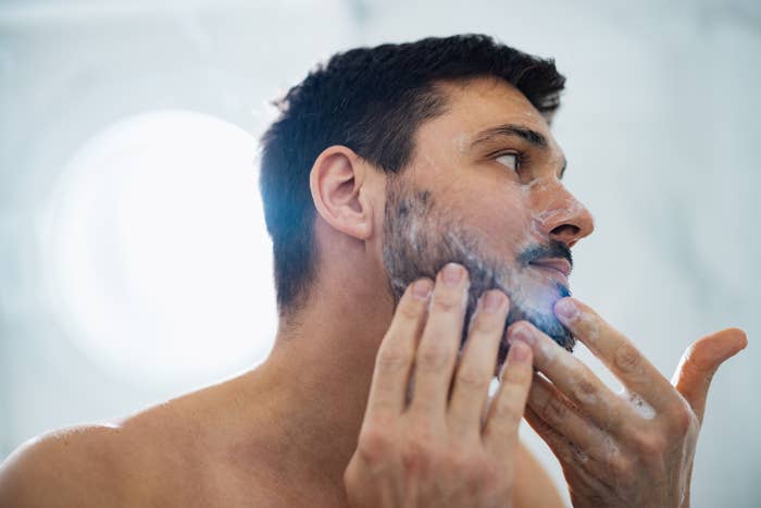 A man applying shaving foam to his face in a bathroom, getting ready to shave