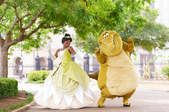 Tiana and Louis from "The Princess and the Frog" happily pose together outdoors, with Louis playfully outstretching his arms