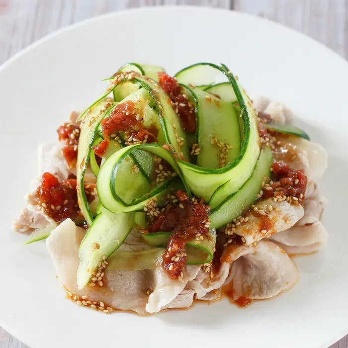 きゅうりの薄切りと肉が盛られた料理。ゴマと赤い調味料がかかっている。