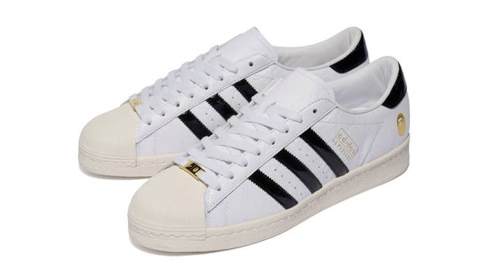 White Adidas Superstar sneakers featuring black stripes on the sides and gold accents on the tongue and heel