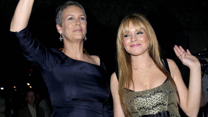 Jamie Lee Curtis in an elegant dress and Lindsay Lohan in a stylish, shimmering outfit wave at an event