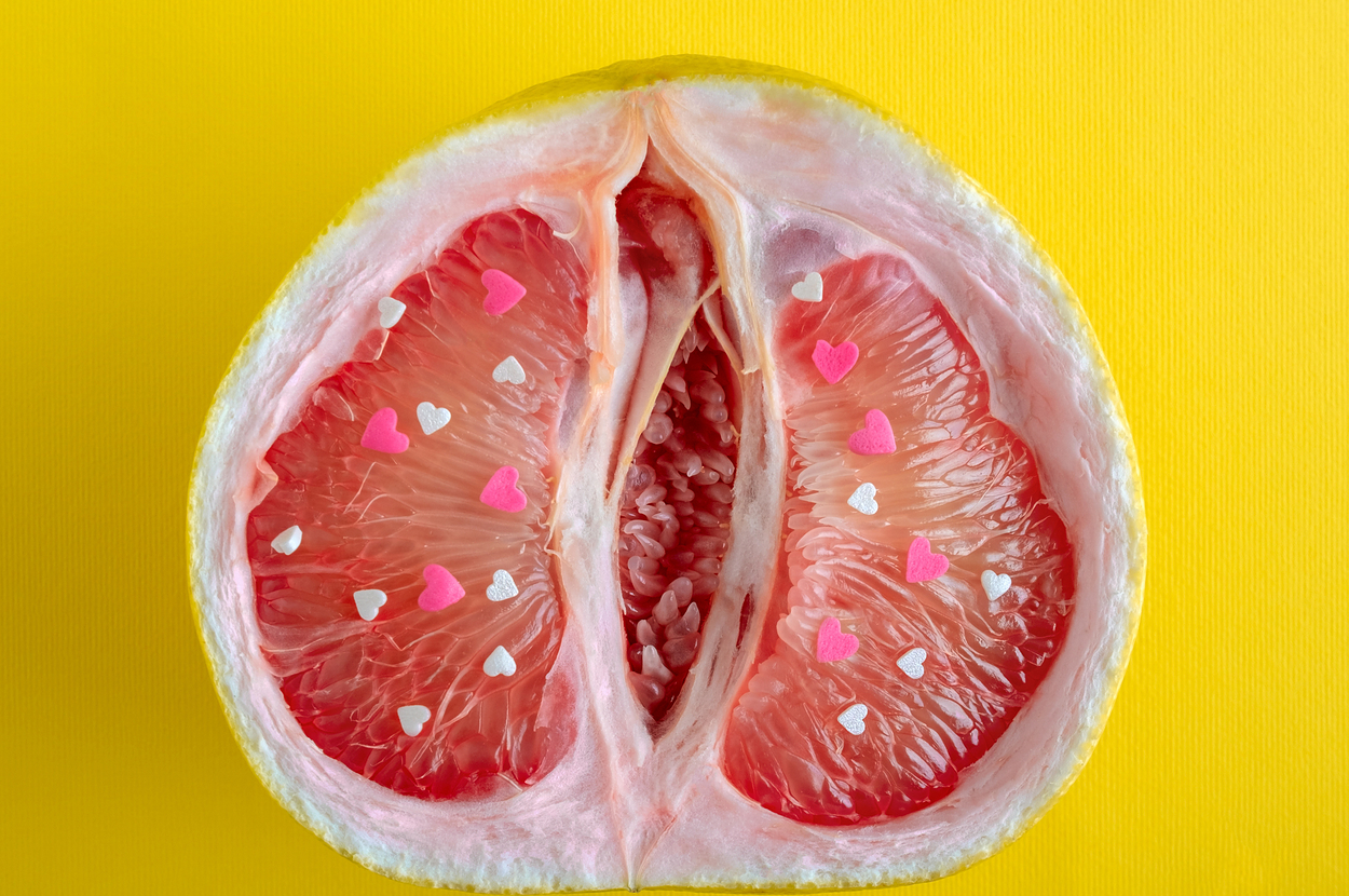 A halved grapefruit with pink and white paper hearts on the segments, set against a yellow background