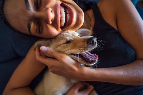 Smiling person cuddles a happy puppy, both with eyes closed, enjoying a joyful moment