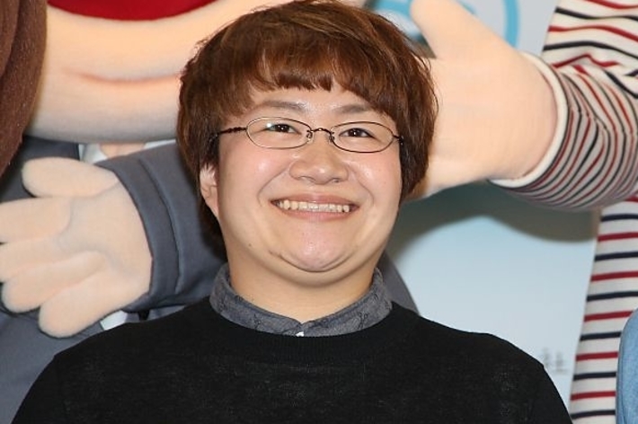 2人の人物が笑顔でポーズをとっている。また、大きなキャラクターの人形が背景にある。