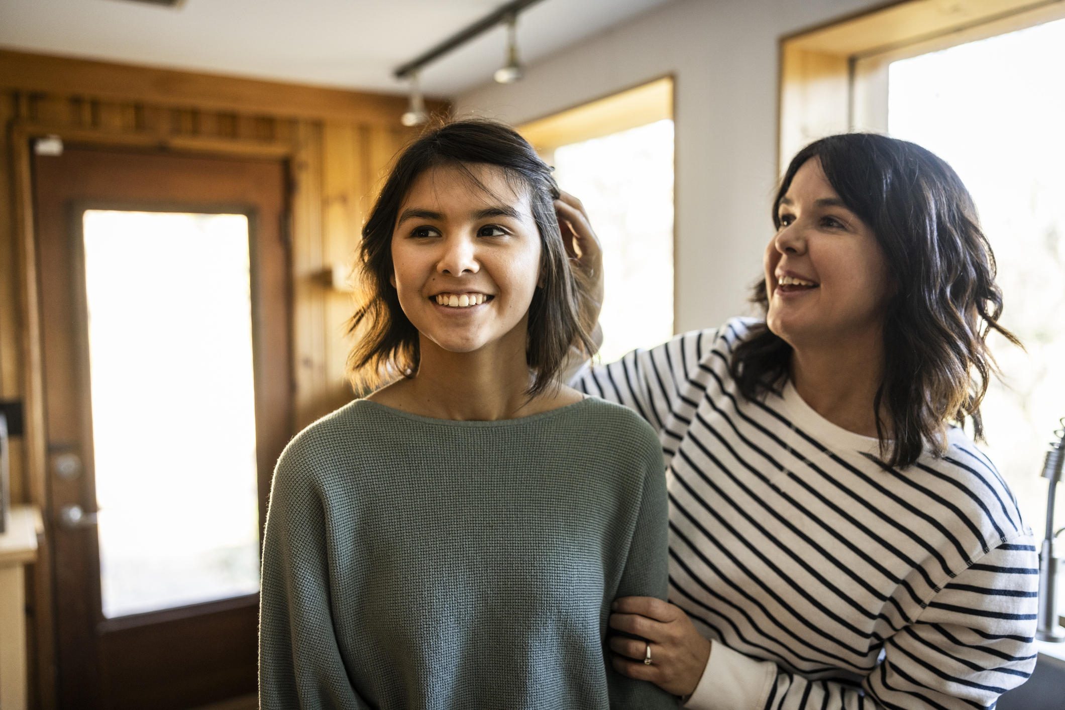 Two women, one in a sweater and another in a striped top, smile as they interact in a cozy, wooden-interior room